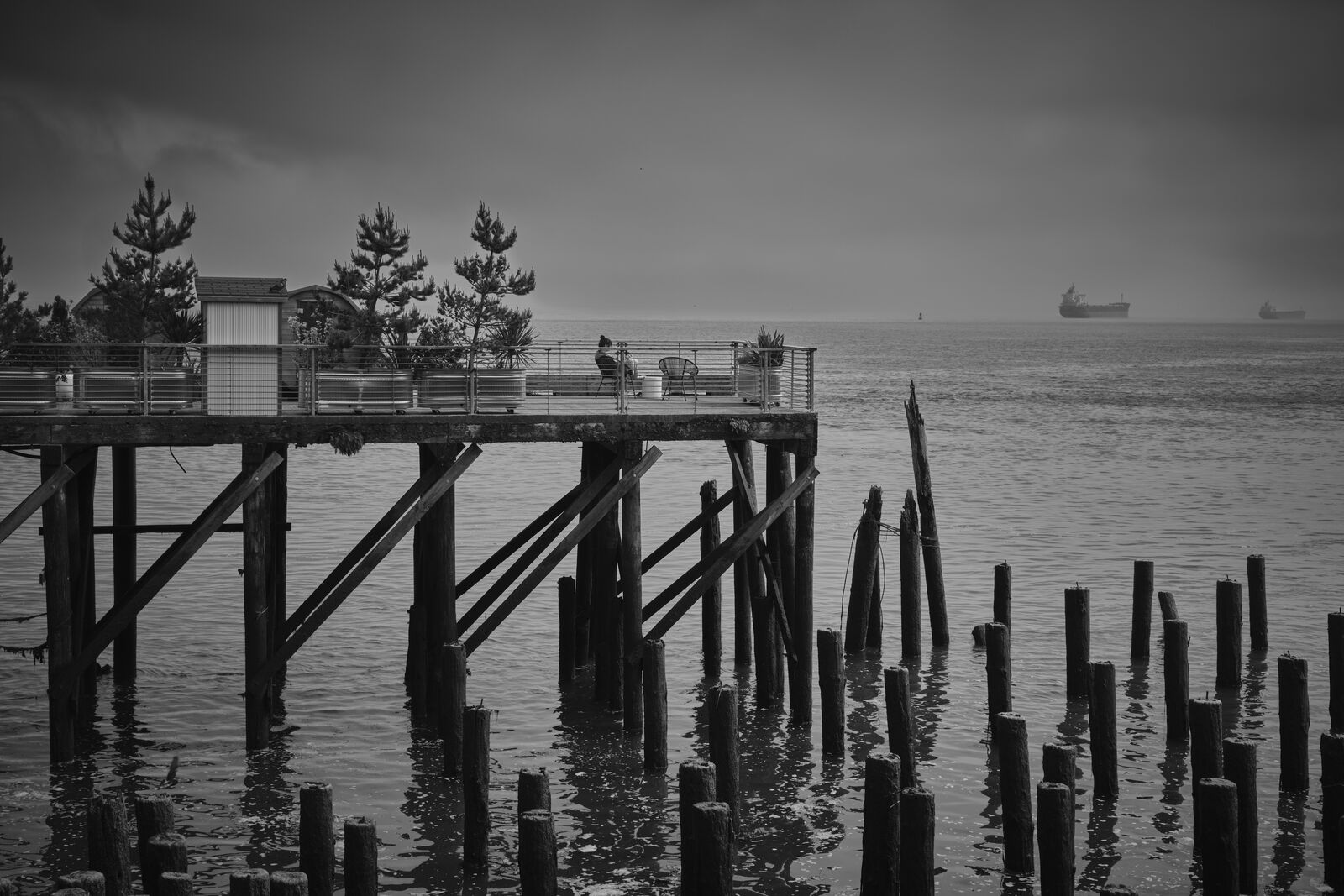 A pier on pilings near downtown Astoria, with freighters at anchor beyond.