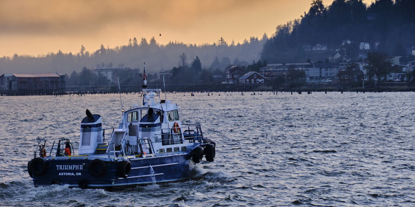 A work boat crosses the river at dawn in front of the Astoria waterfront.